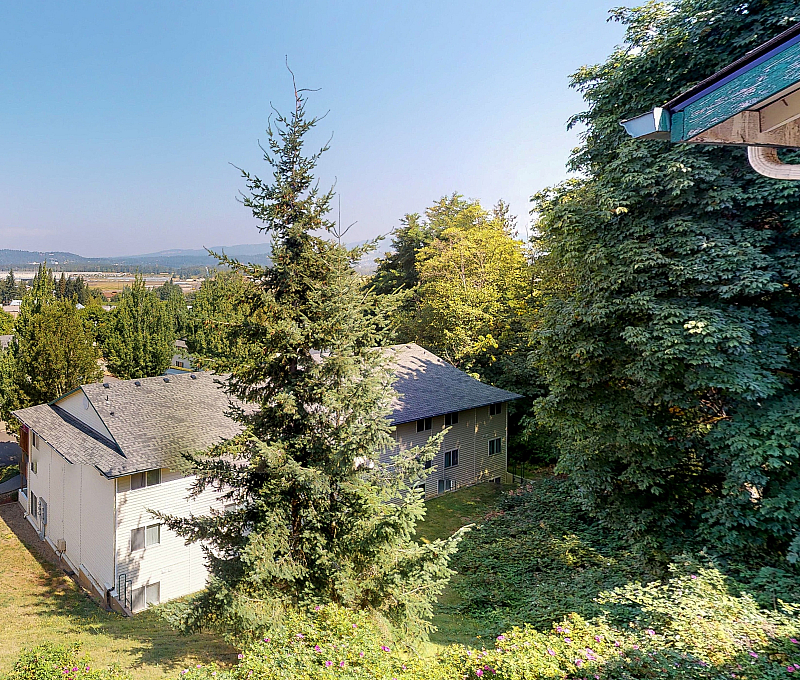 Scenic view from an apartment window showcasing surrounding greenery, rooftops, and distant mountains under a clear blue sky.