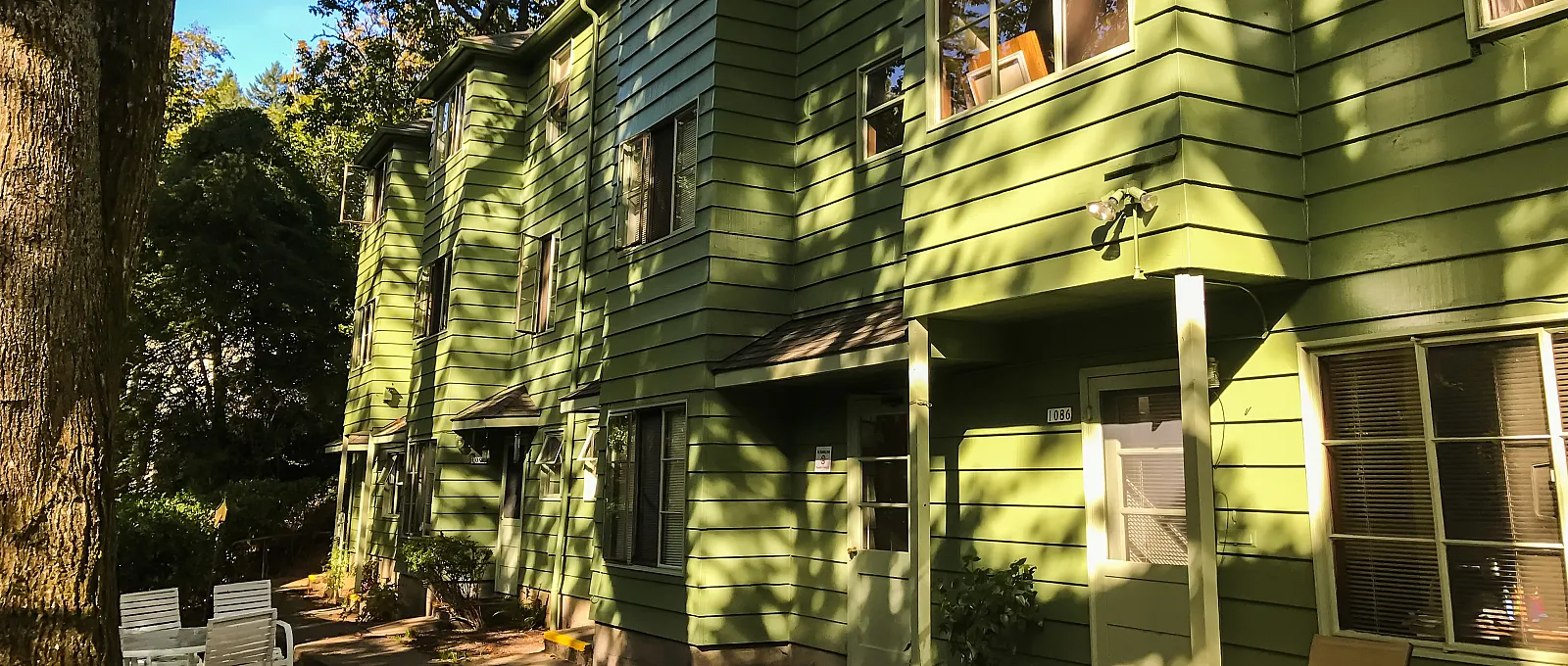 Charming apartment complex with fresh green exterior surrounded by lush trees and inviting outdoor seating area.