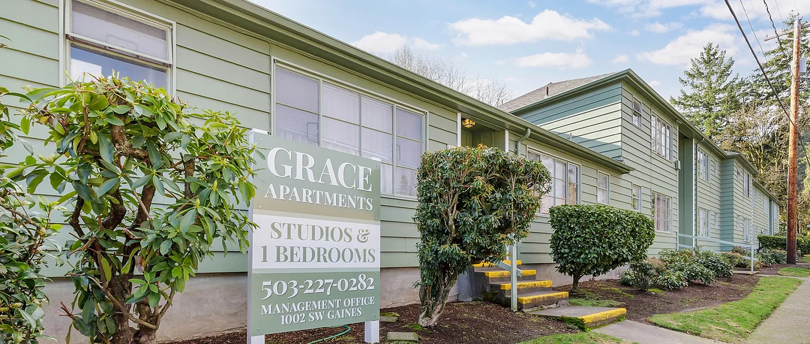 Charming Grace Apartments with lush greenery, offering studio and 1-bedroom units in a serene, tree-lined setting.