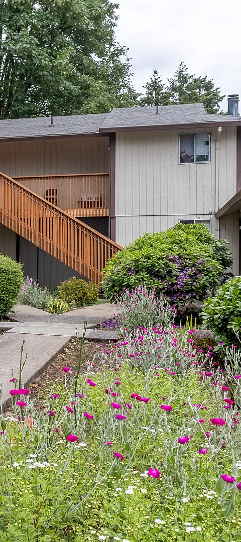 Charming apartment complex with lush landscaping, vibrant flowers, and inviting pathways leading to cozy residences.
