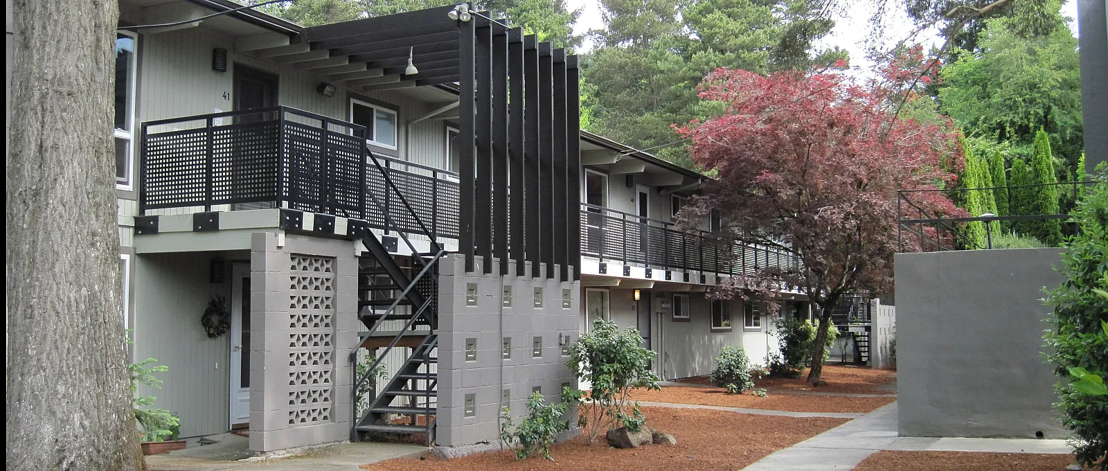 Charming two-story apartment building surrounded by lush greenery and natural beauty, featuring modern balcony railings and inviting outdoor space.