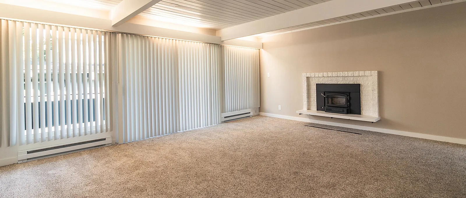 Bright and spacious living room with cozy carpet, elegant fireplace, and large windows with modern blinds.