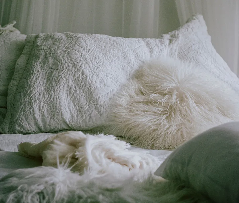 Inviting and cozy bedroom with plush white pillows and a chic fur accent on a soft bed, exuding warmth and elegance.