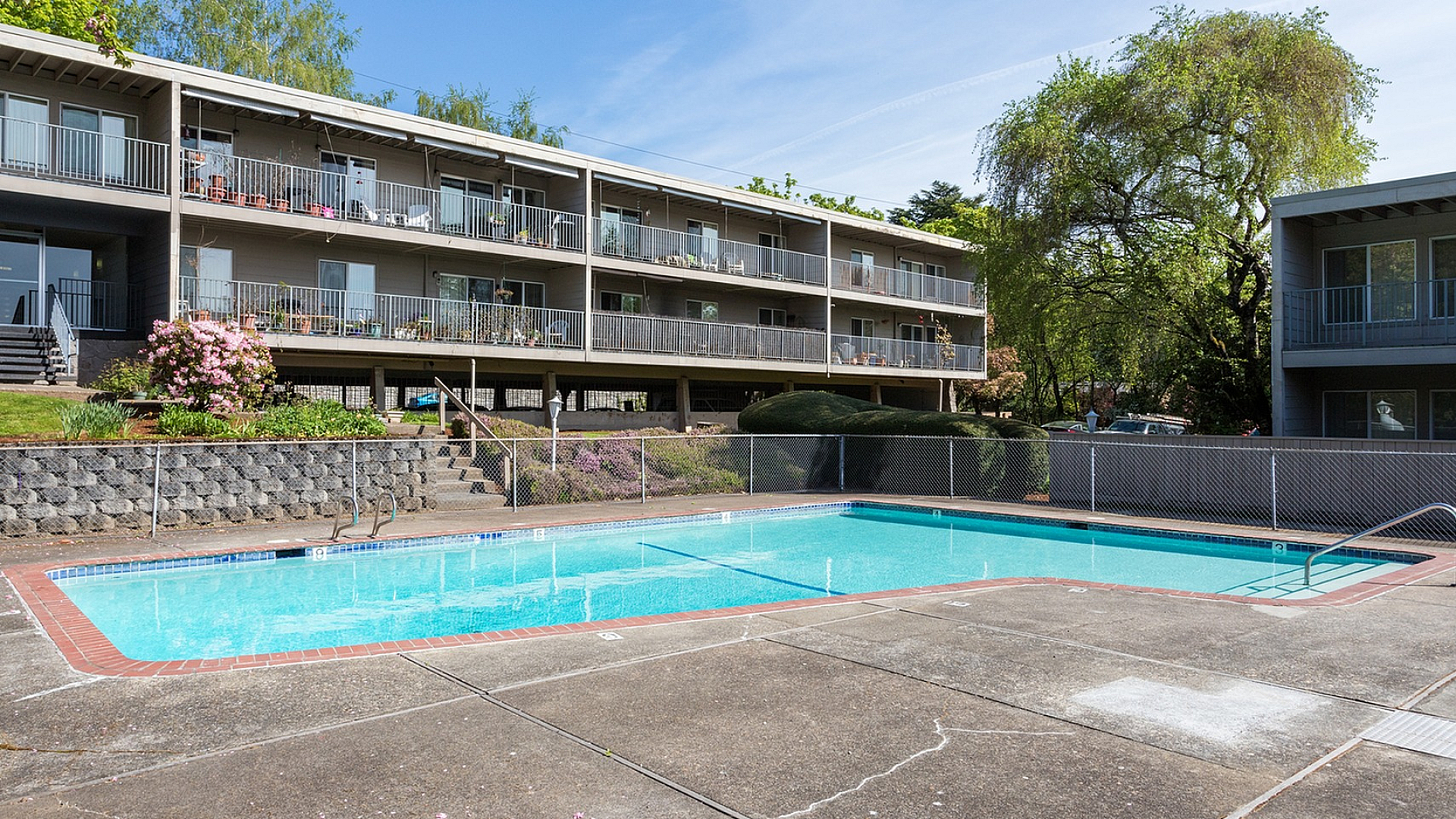 Charming apartment complex with a serene outdoor pool area, surrounded by lush greenery and modern balconies.
