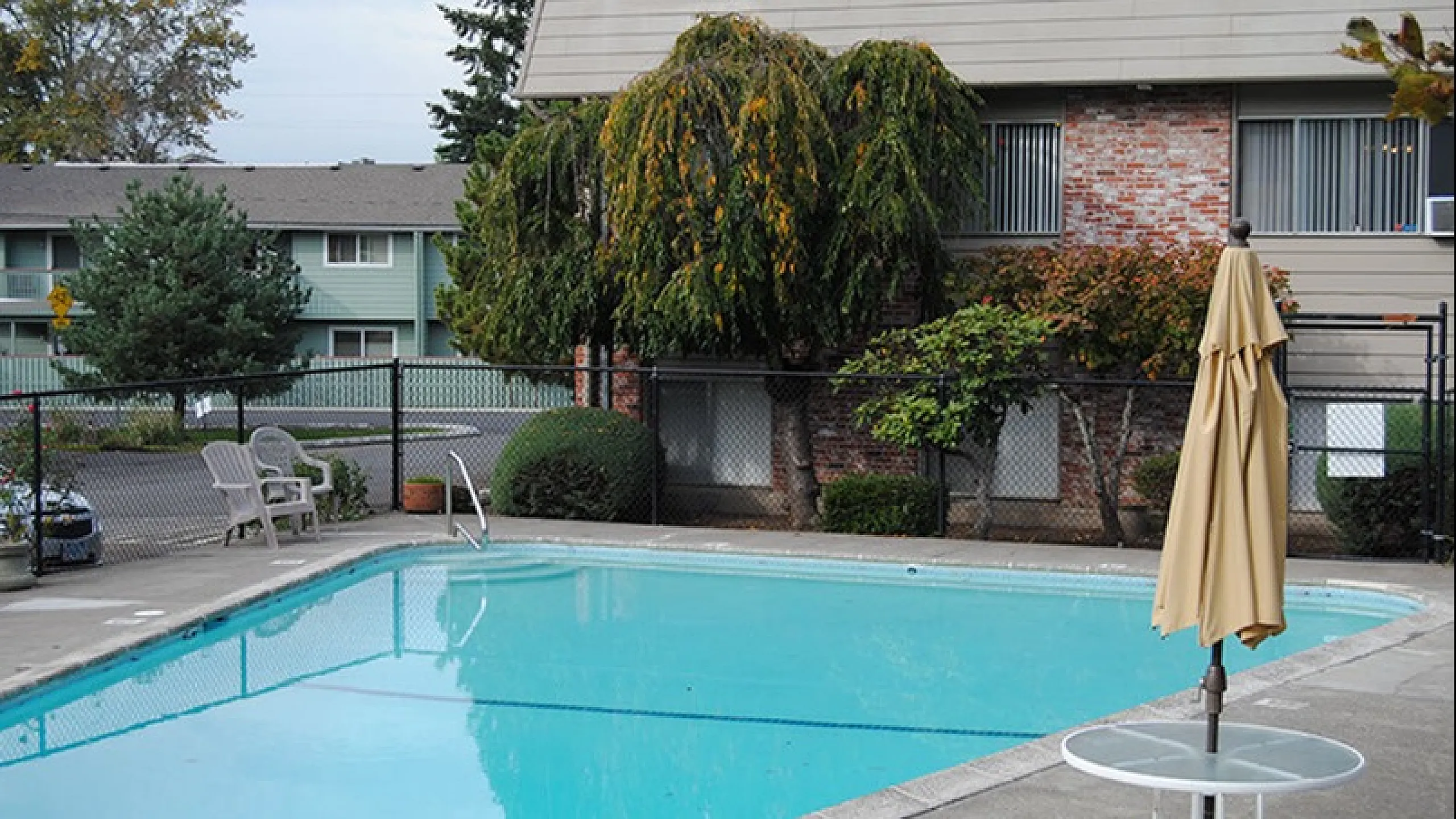 Inviting outdoor pool area with seating, surrounded by lush greenery and a charming apartment complex.