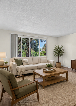 Beautifully staged living room with modern furnishings, featuring a cozy sofa, stylish armchairs, and a large window offering lush green views.
