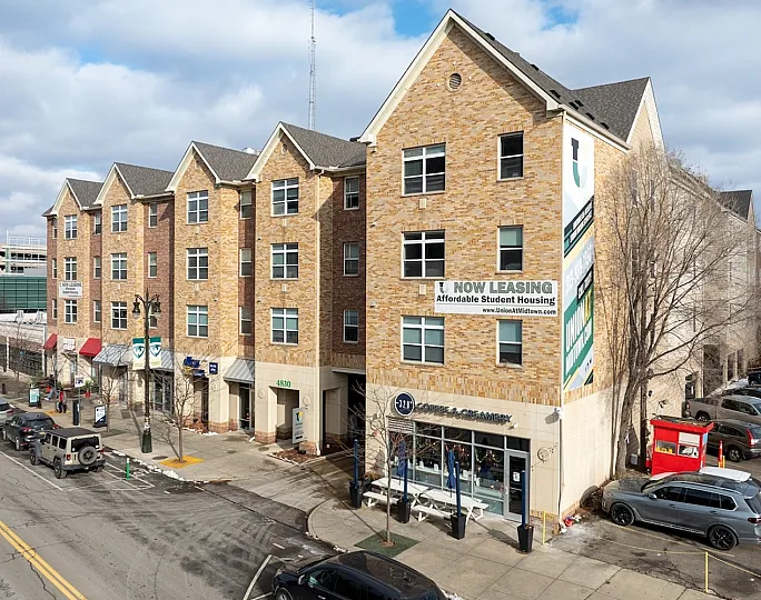 Modern brick apartment building offering affordable student housing, featuring a vibrant street view with cafes and parking.