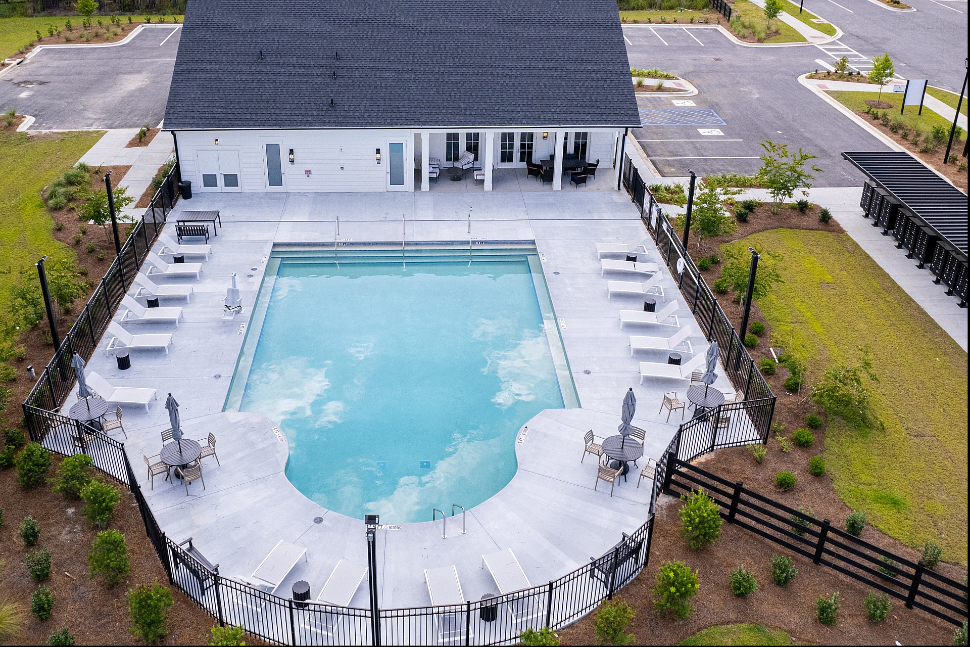 Elegant aerial view of a modern apartment complex pool area with luxurious lounge chairs and umbrellas, surrounded by lush greenery.