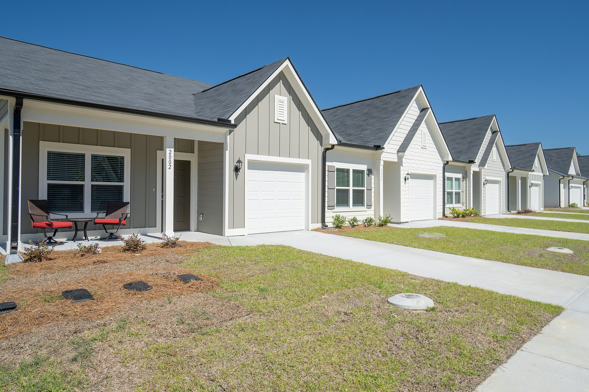 Charming row of modern townhouses with inviting patio seating, showcasing stylish design and neatly landscaped gardens under a clear blue sky.