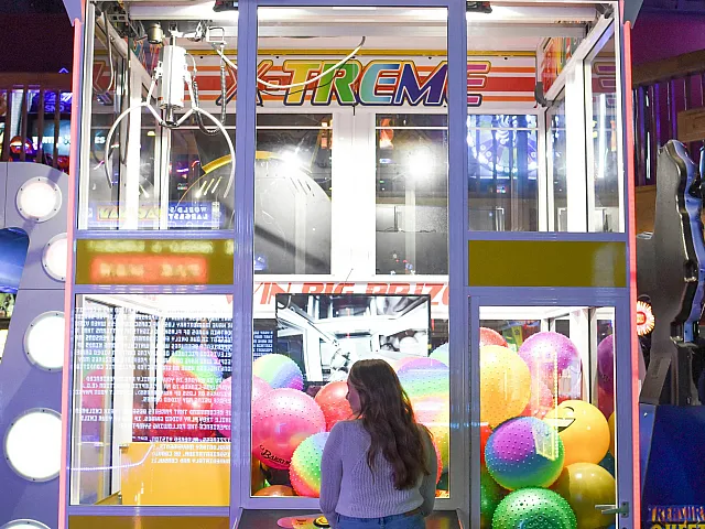 Exciting arcade crane game with vibrant colorful balls and a player eagerly trying their luck.