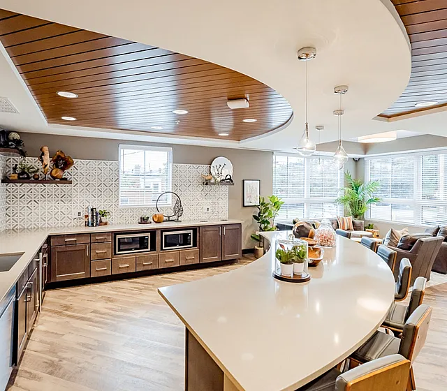 Contemporary open-concept community lounge with stylish curved countertop, elegant lighting, and cozy seating area surrounded by large windows.