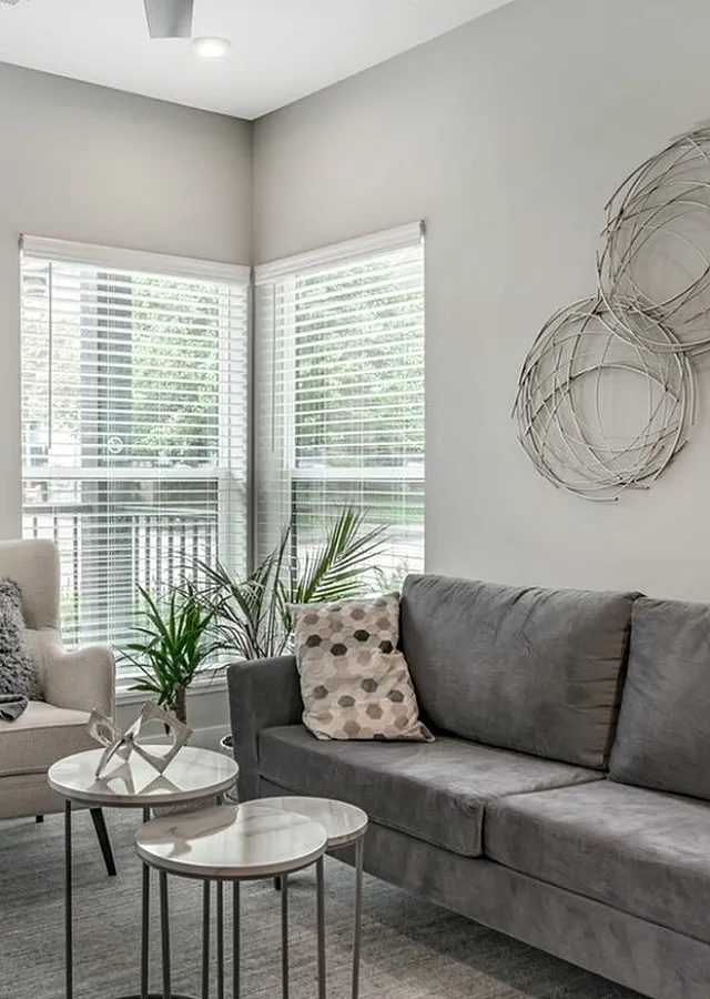 Contemporary living room with a cozy gray sofa, stylish armchair, and artistic wall decor, framed by large windows bringing in natural light.
