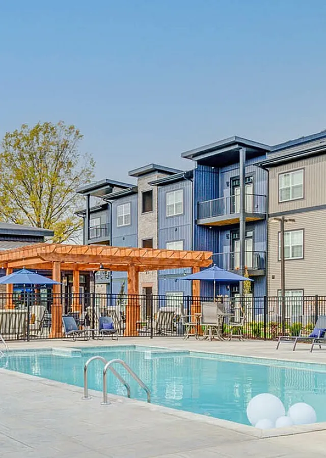 Modern apartment complex with a sparkling pool, elegant seating areas, and vibrant blue umbrellas offering a luxurious outdoor experience.