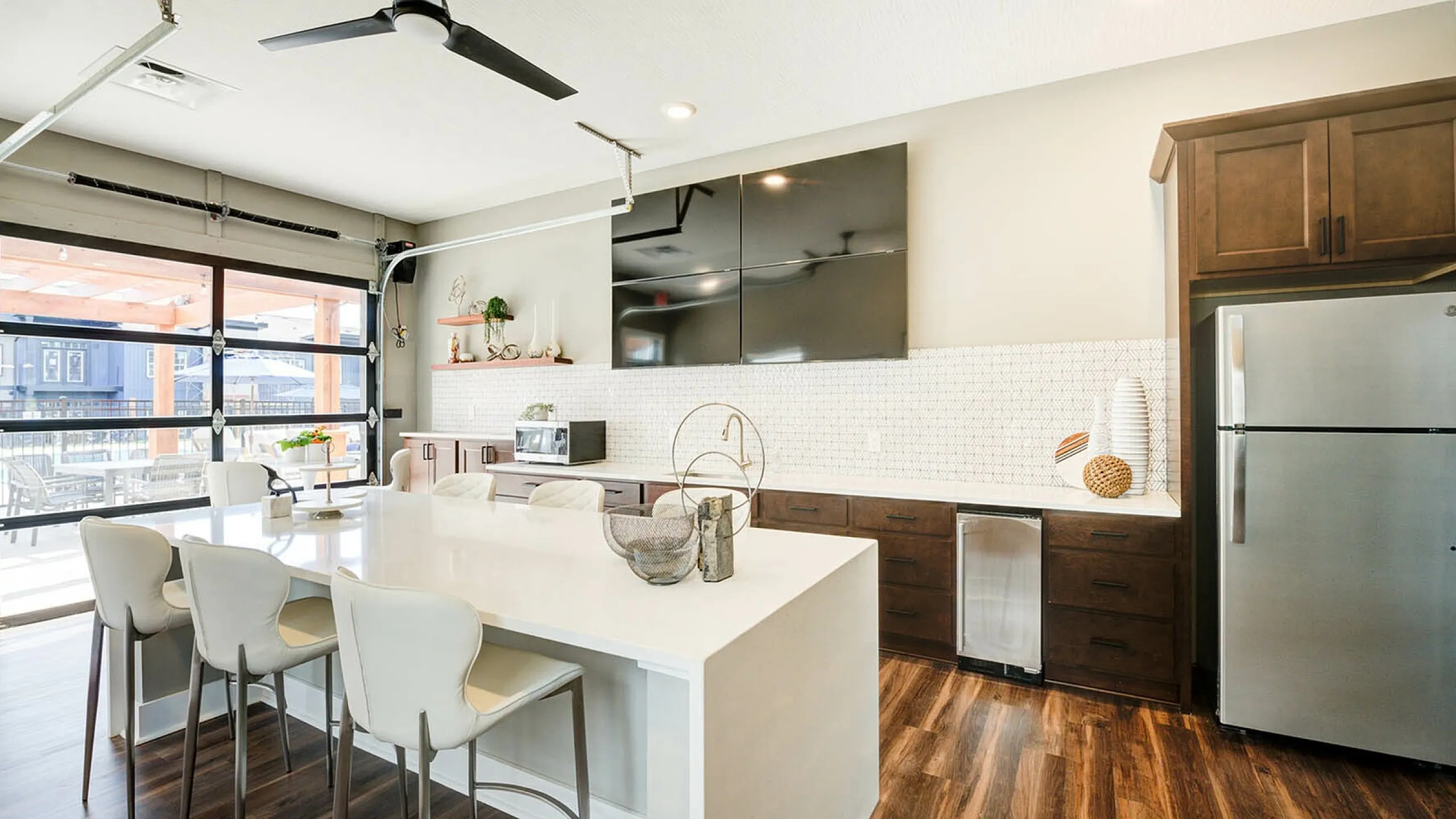 Modern kitchen with sleek white island, stylish bar stools, and natural light from large windows.