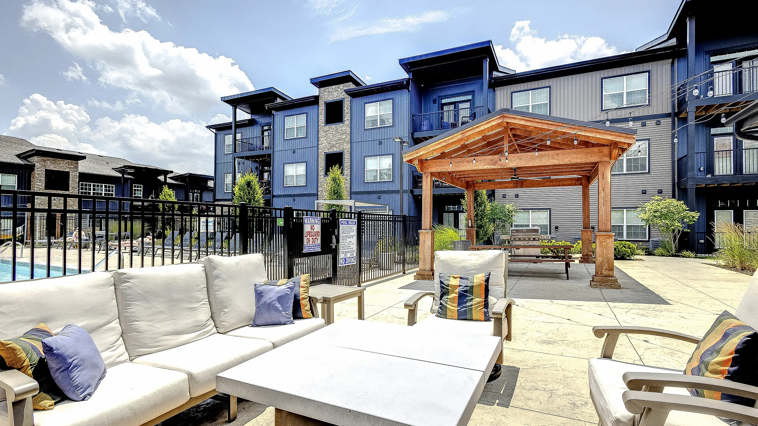 Charming apartment complex with modern outdoor seating area, featuring a cozy gazebo surrounded by lush landscaping and stylish architecture.