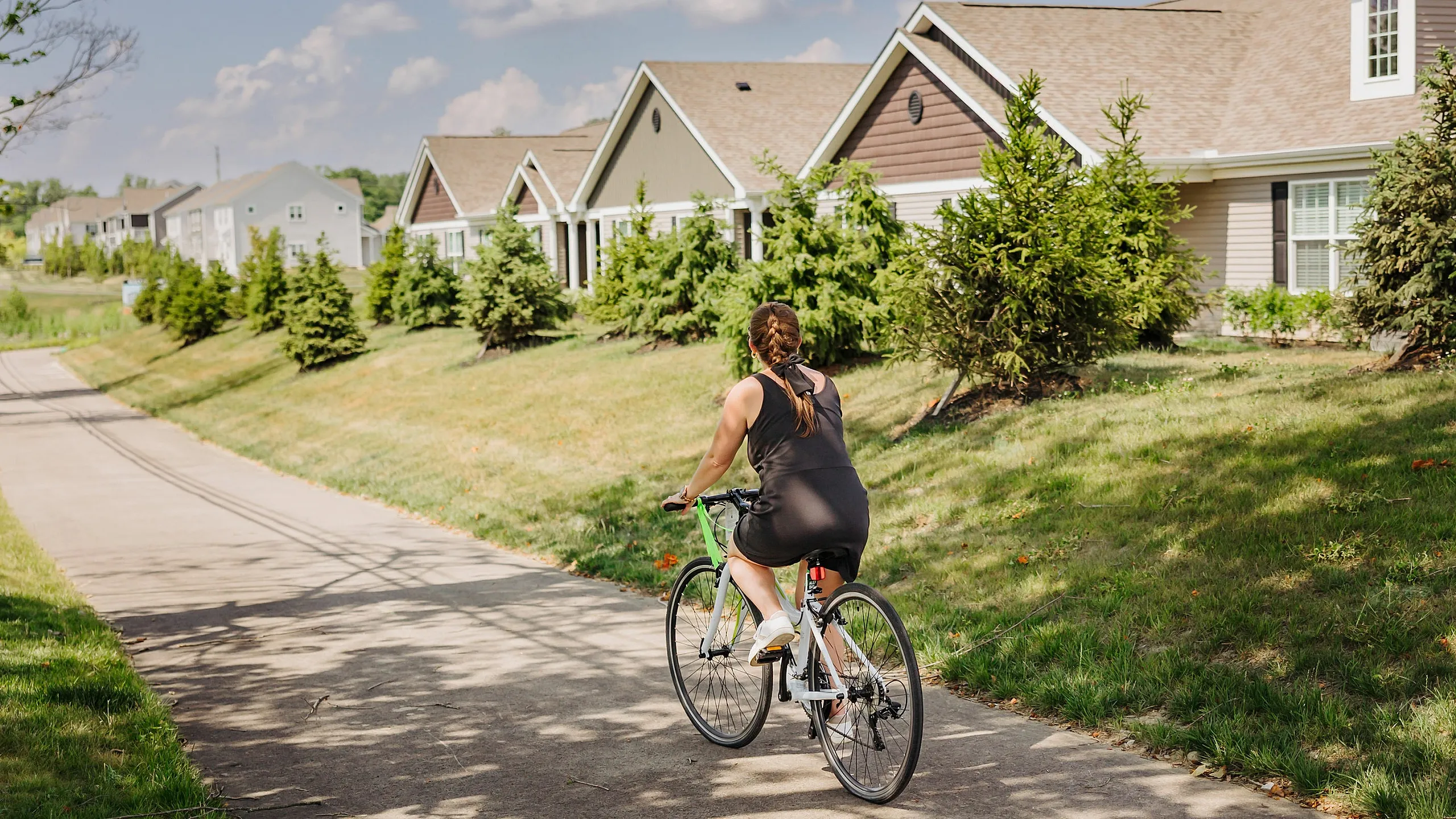 Idyllic suburban scene with a cyclist enjoying a sunny day on a paved path lined with charming houses and lush greenery.