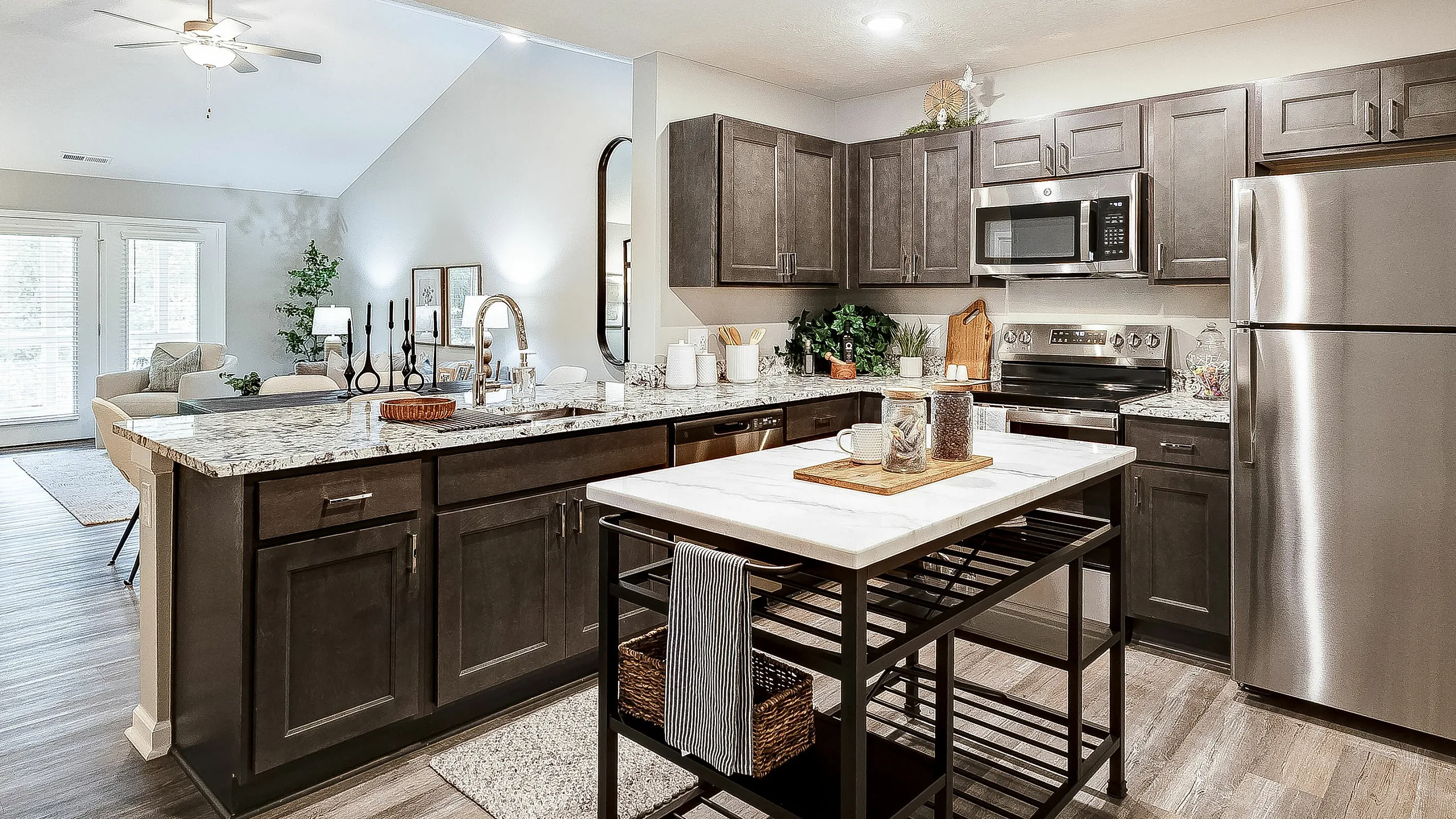 Modern open-concept kitchen with sleek stainless steel appliances, elegant dark cabinetry, and a chic marble island, flowing seamlessly into a bright living area with stylish decor.