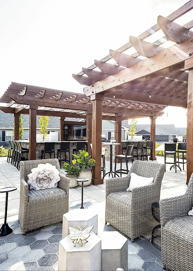 Elegant outdoor patio with stylish wicker seating, a wooden pergola, and modern bar area, perfect for relaxing and entertaining.
