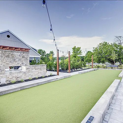 Elegant outdoor space featuring a well-maintained bocce ball court, surrounded by lush greenery and stylish stone walls with string lights overhead.