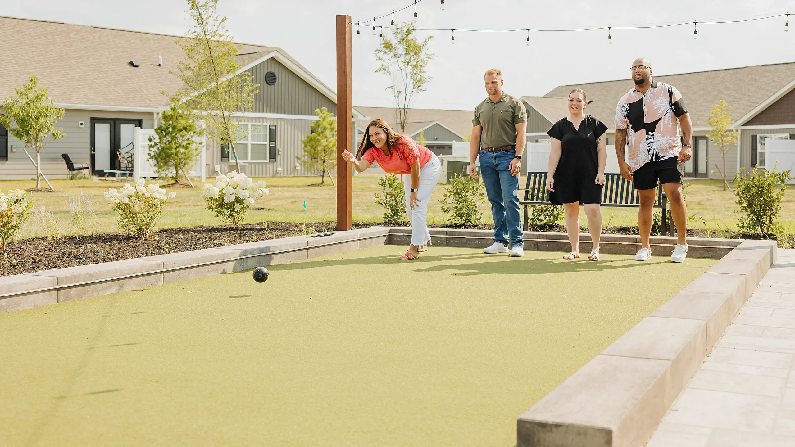 Vibrant community living with residents enjoying a bocce ball game on a sunny day, surrounded by charming cottages and lush greenery.