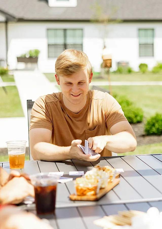 Young man enjoying a sunny day playing cards outdoors with friends, complete with refreshing drinks and snacks on the table.