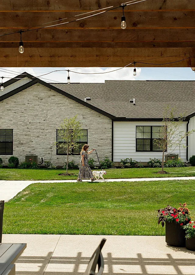 Charming suburban scene featuring a woman walking her dog by a modern apartment complex with a picturesque lawn and lush greenery.