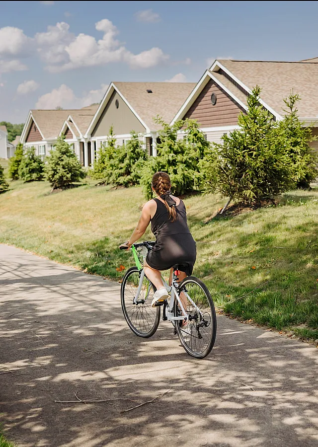 Charming suburban scene with a cyclist enjoying a sunny day on a lush green pathway, flanked by picturesque houses and vibrant landscaping.