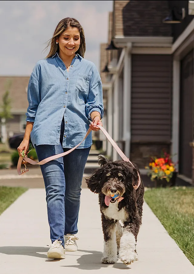 Smiling woman joyfully walking her dog on a sunny day in a charming suburban neighborhood.