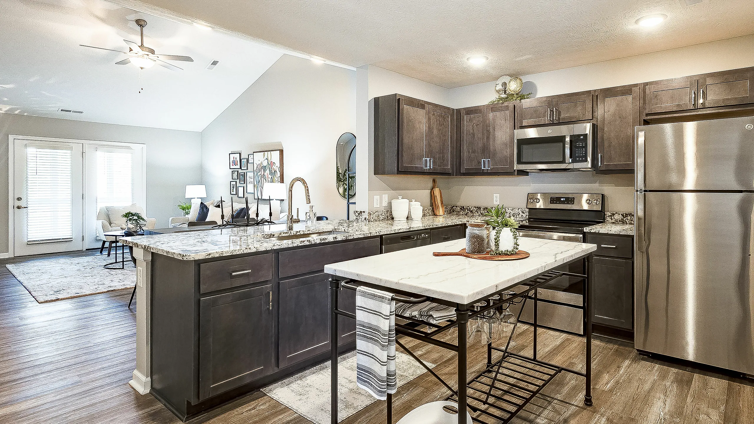 Modern open-concept kitchen and living area featuring sleek stainless steel appliances, granite countertops, and elegant wood flooring, bathed in natural light.