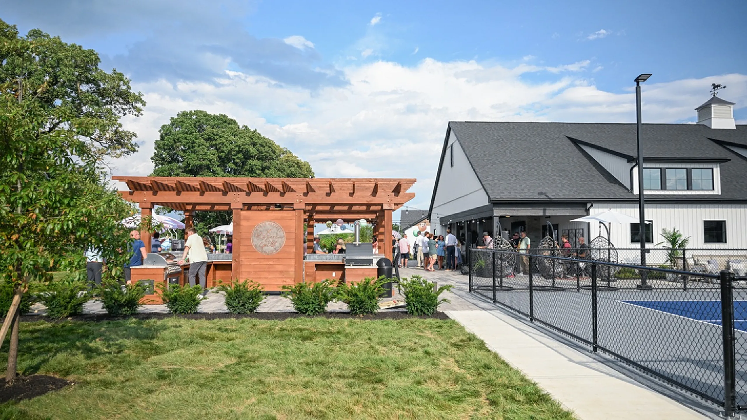 Charming outdoor space with a wooden pergola and lively gathering near a modern building, perfect for social events and community activities.
