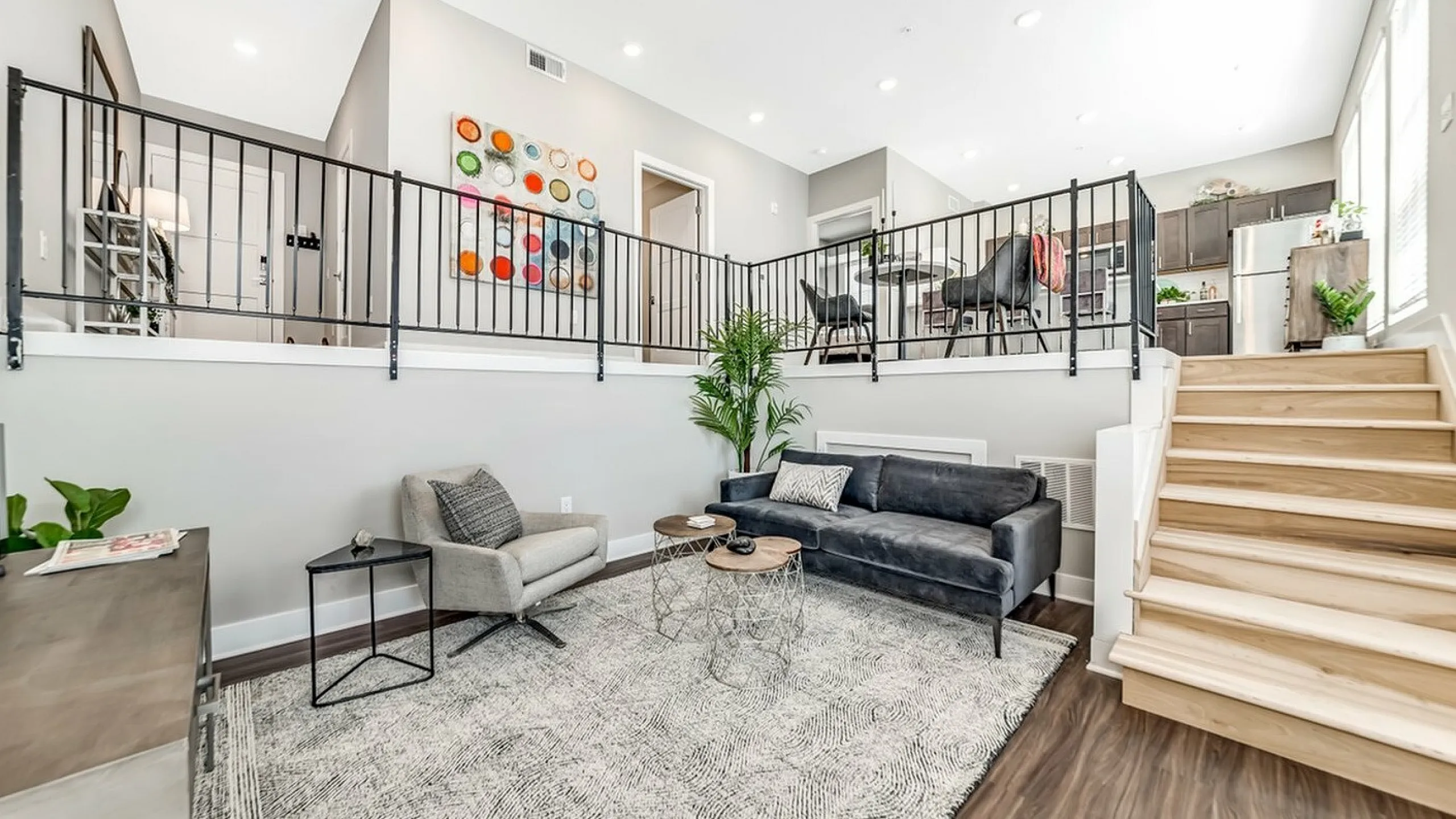 Bright and airy living space with modern split-level design, featuring elegant seating, lush greenery, and sleek kitchen area.
