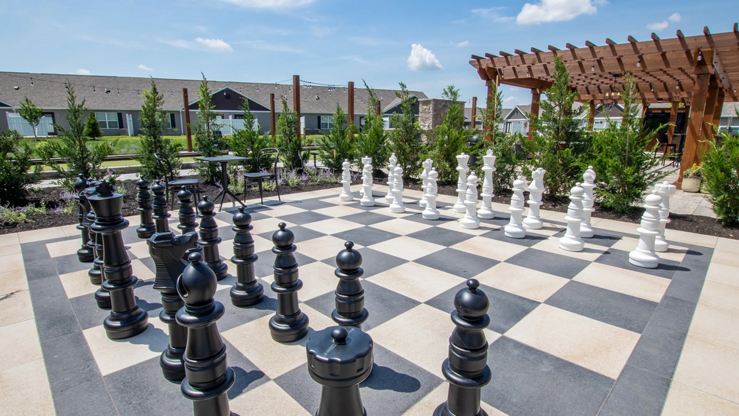 Expansive outdoor chess area with large pieces, surrounded by lush greenery and a stylish pergola, offering a perfect spot for relaxation and strategic play.