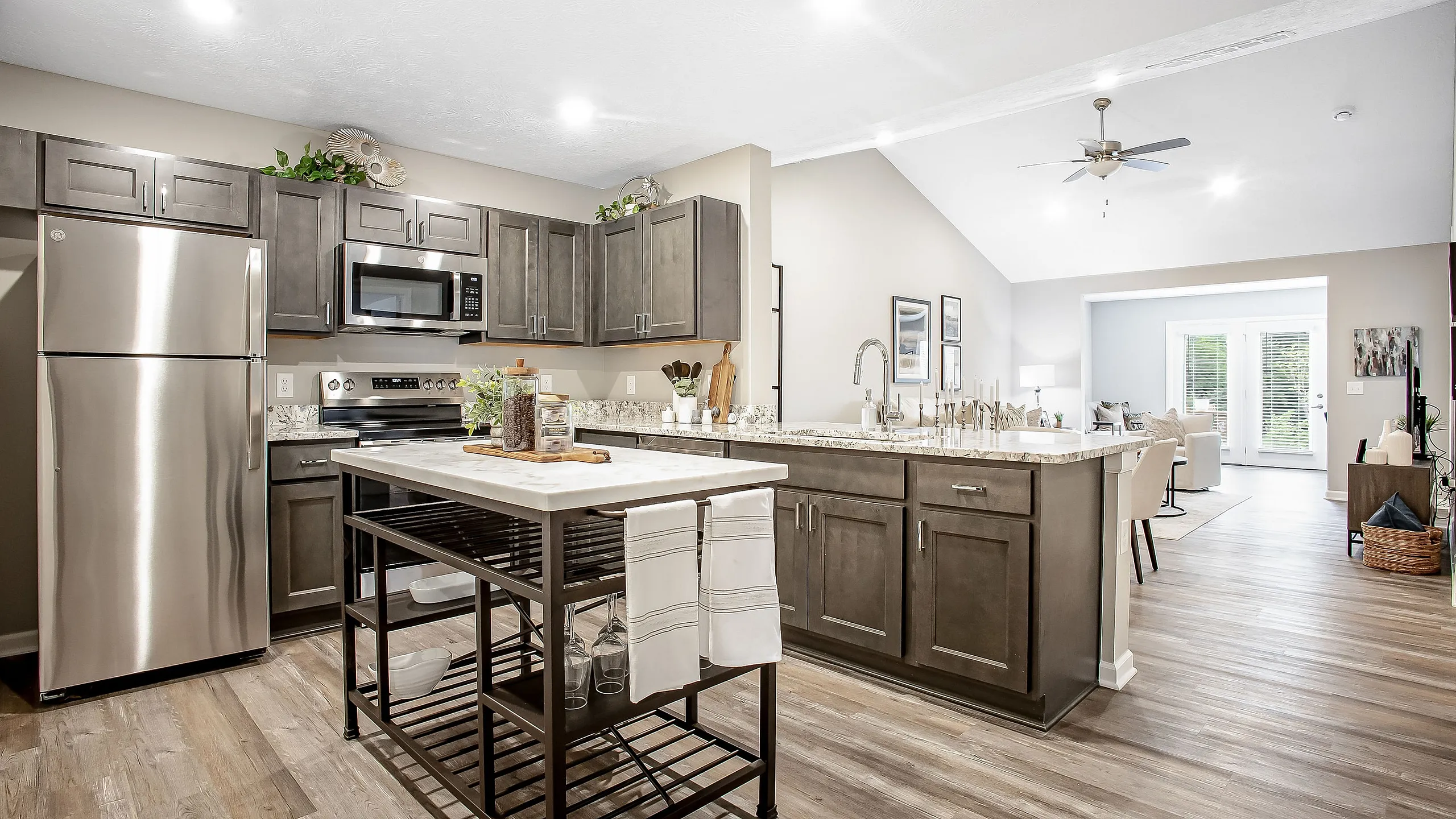 Modern open-concept kitchen with sleek stainless steel appliances, elegant cabinetry, and a central island flowing seamlessly into a bright living area with large windows.