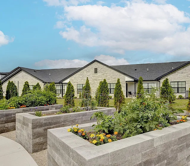 Charming single-story residence with lush garden beds and a modern stone facade under a clear blue sky.