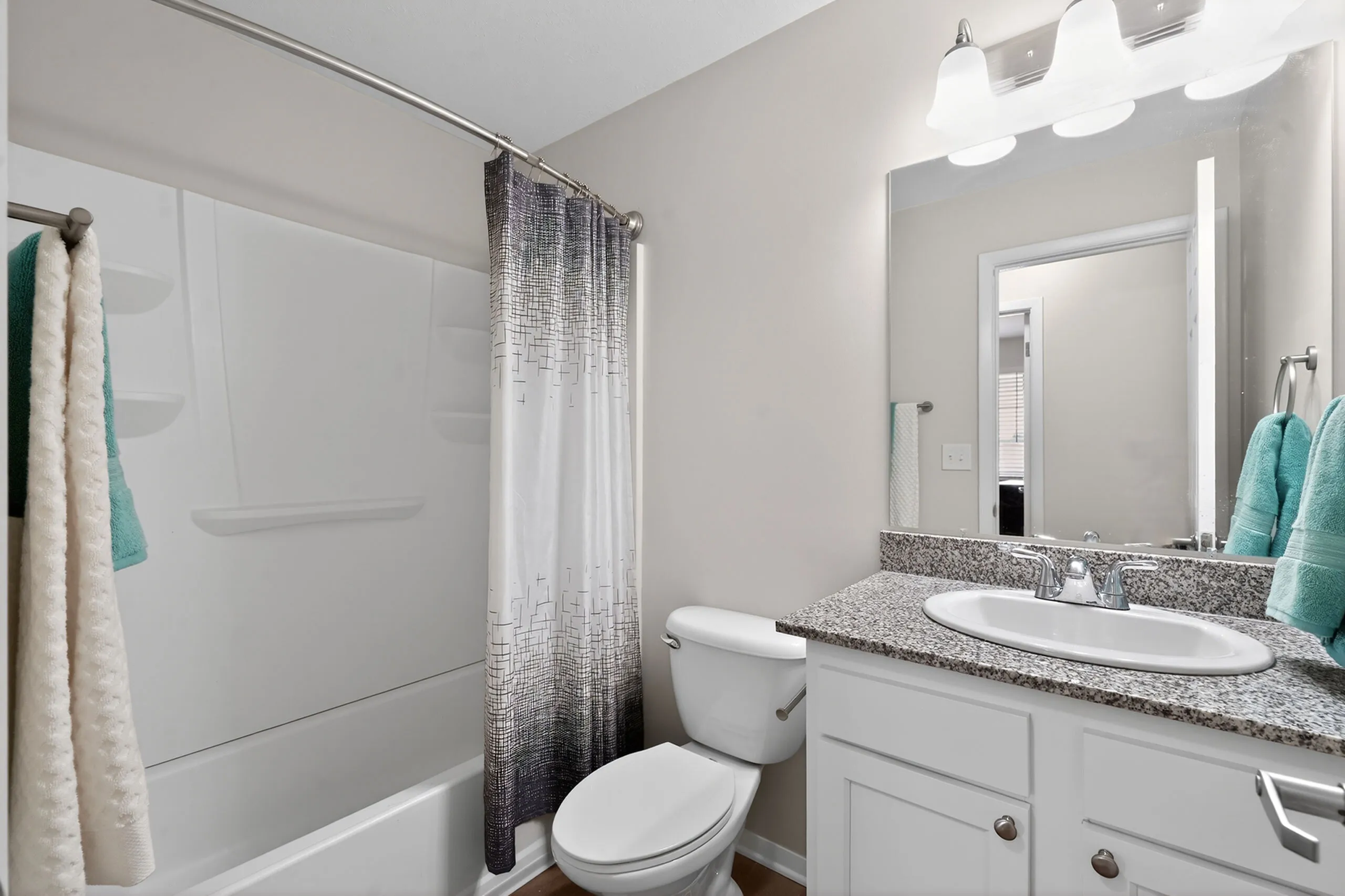 Contemporary bathroom with elegant granite countertop, chic lighting, and modern bathtub featuring a stylish shower curtain.