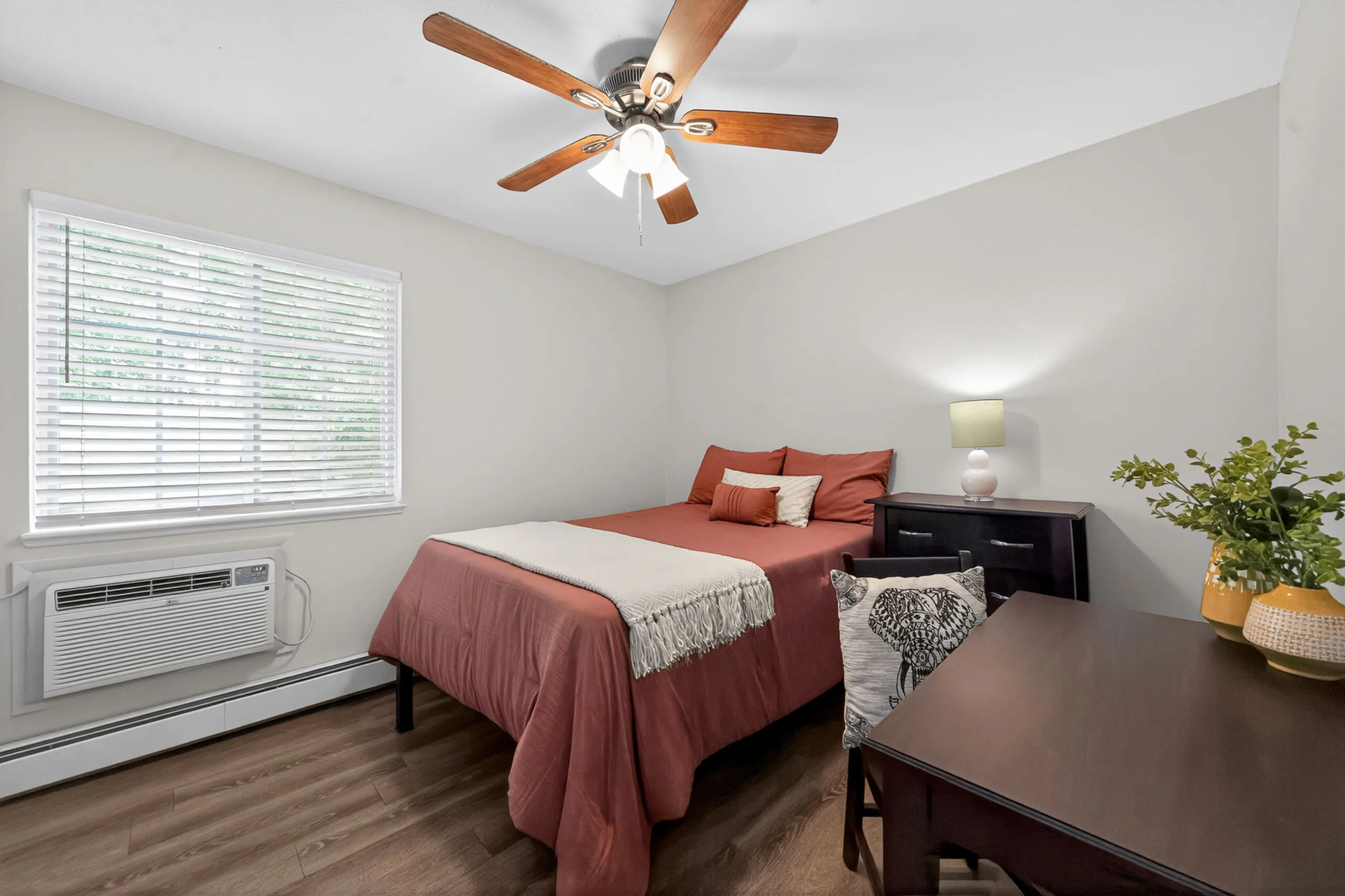 Cozy bedroom with a wooden floor, featuring a comfortable double bed, ceiling fan, and chic decor.