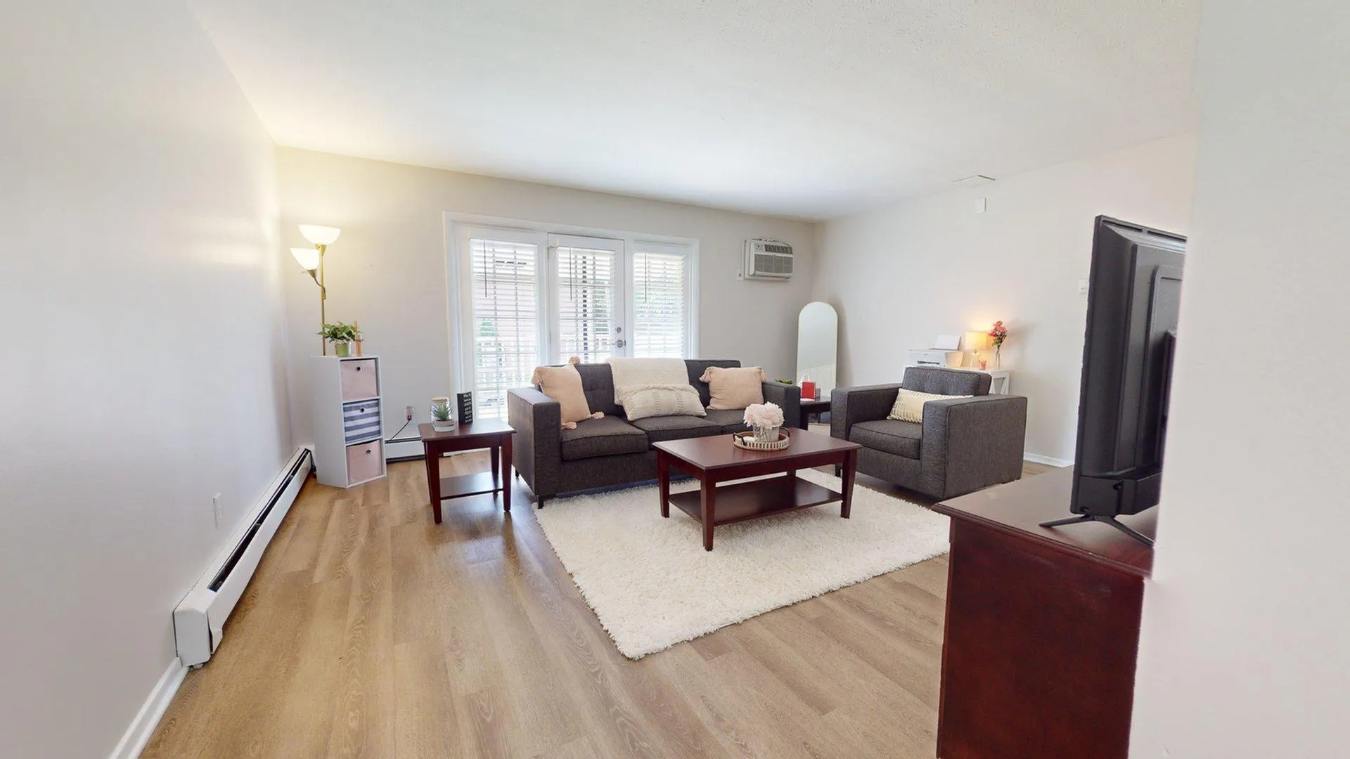 Bright and inviting living room with modern gray sofas, cozy white rug, and sleek wooden tables, enhanced by natural light from large windows.