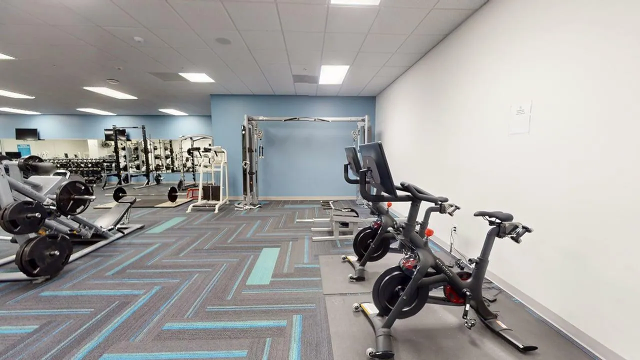 Modern fitness center featuring state-of-the-art gym equipment, including exercise bikes and weightlifting machines, in a spacious and well-lit environment.