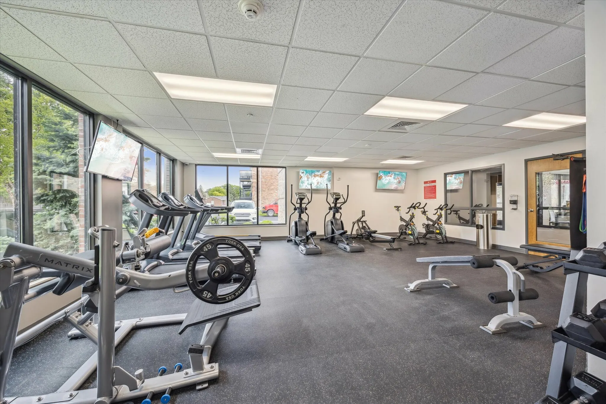 Bright and modern fitness center featuring state-of-the-art exercise equipment, including treadmills, ellipticals, and weight machines, with large windows providing natural light and outdoor views.