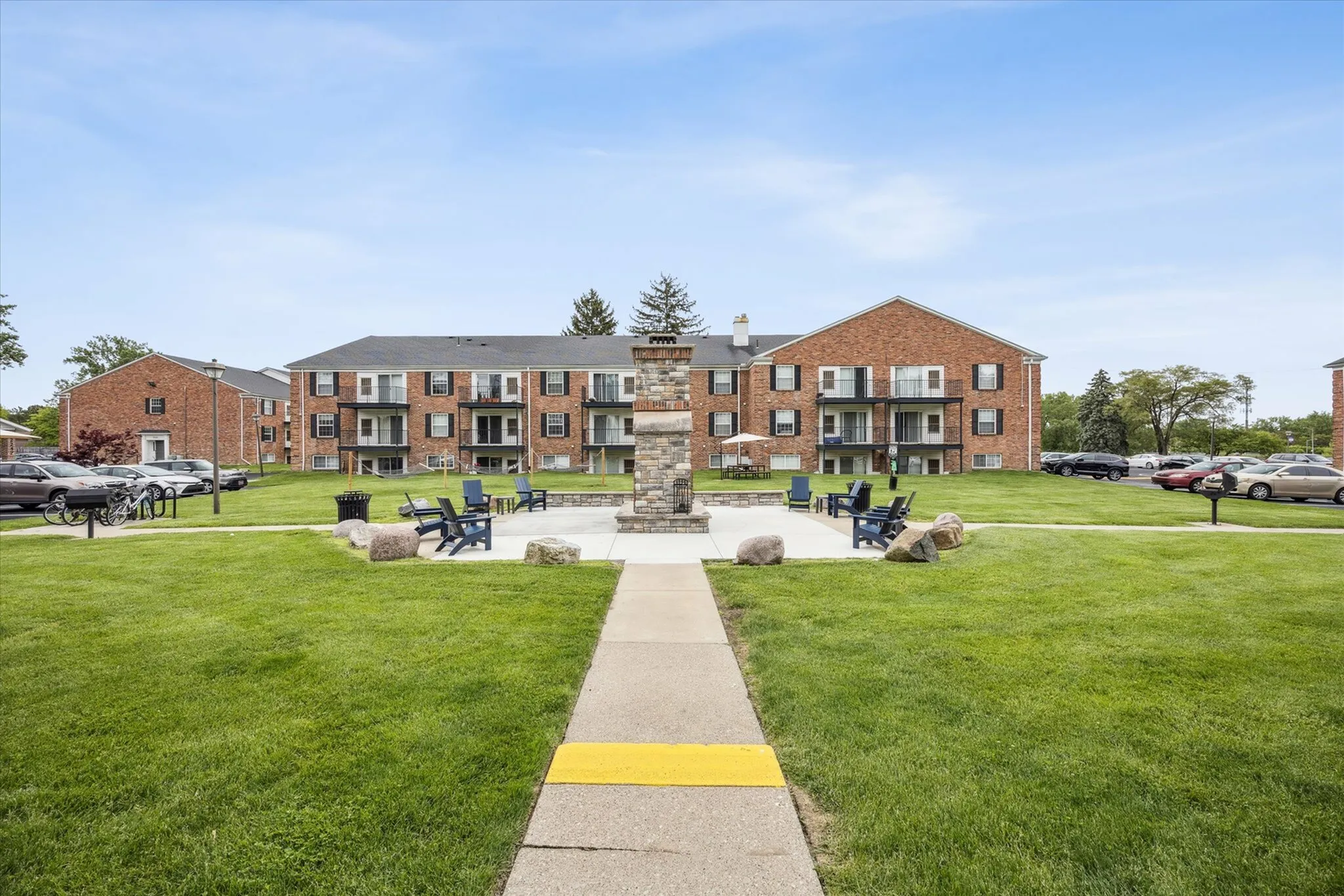 Inviting apartment complex with red brick facade, featuring spacious balconies, well-maintained green lawn, and outdoor seating around a cozy fire pit.