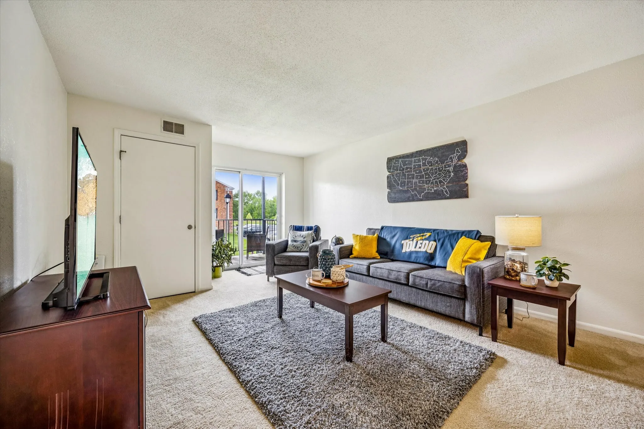 Inviting living room with plush gray sofa, vibrant yellow accents, and floor-to-ceiling windows leading to a scenic balcony.