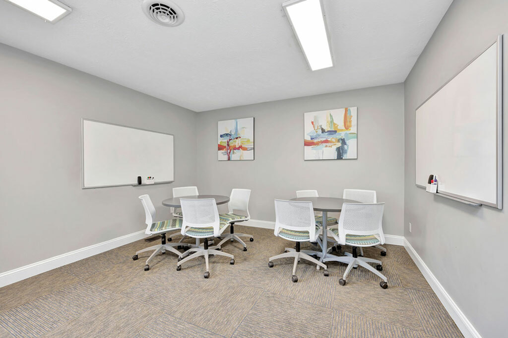Modern conference room with round tables, ergonomic chairs, abstract art, and whiteboards, perfect for creative meetings.