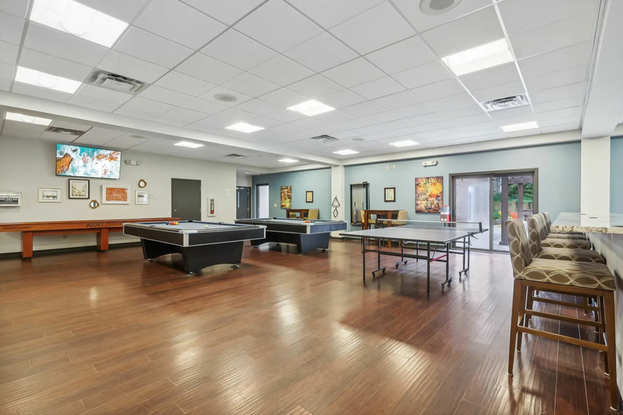 Spacious recreation room featuring elegant wood flooring, billiard tables, and seating area with modern decor and natural light.