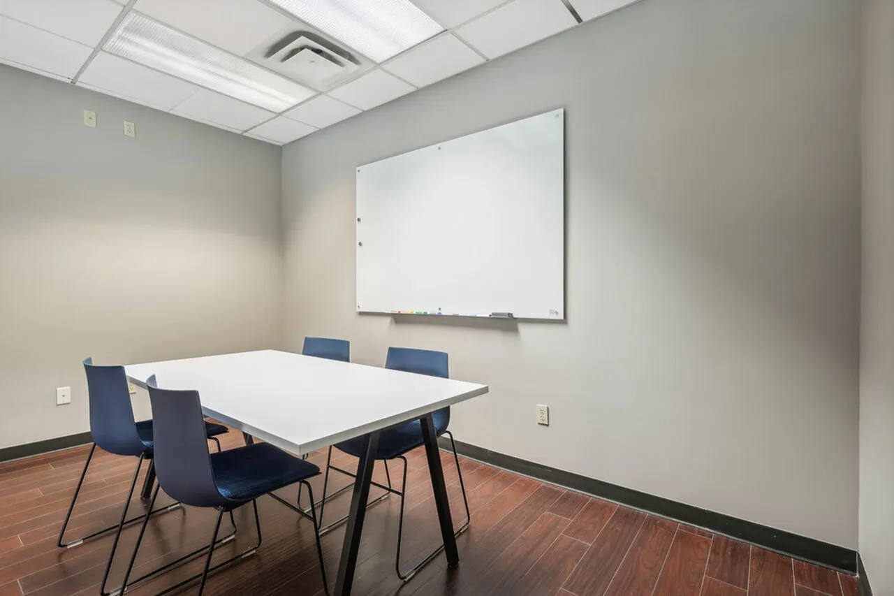 Bright and modern meeting room with sleek white table, blue chairs, and a large whiteboard, perfect for collaborative work.