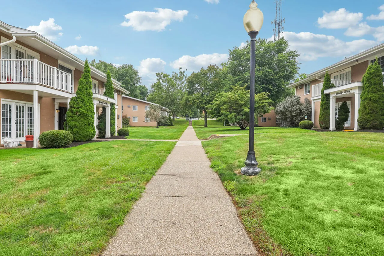 Charming apartment complex with manicured lawns, stylish balconies, and scenic walkway under bright blue skies.