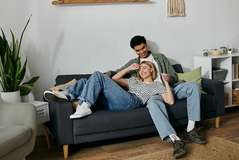 Cozy living room with a stylish couple relaxing on a modern grey sofa, surrounded by chic decor and lush greenery.