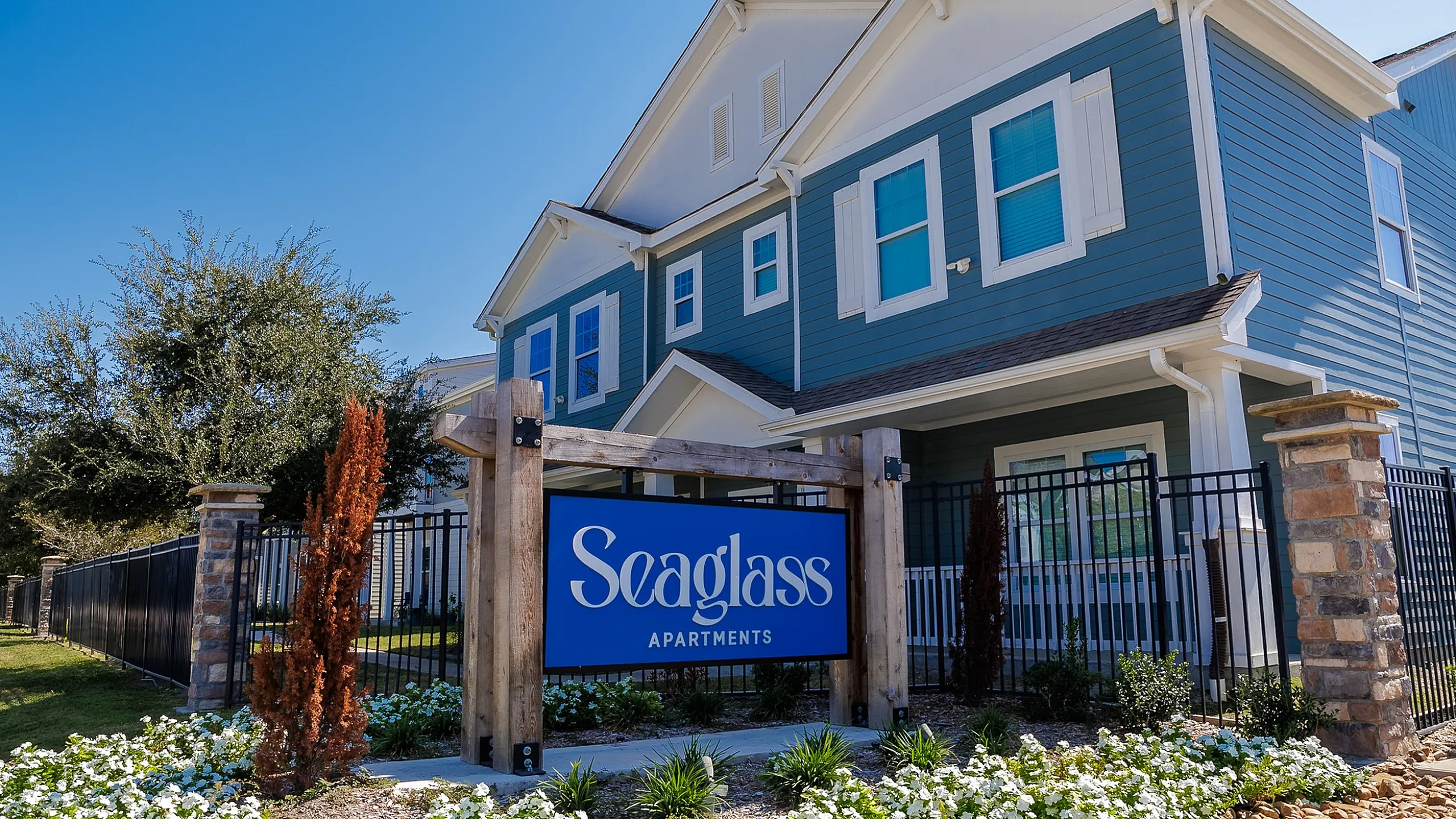 Inviting two-story apartment building with charming blue facade and lush landscaping at Seaglass Apartments.