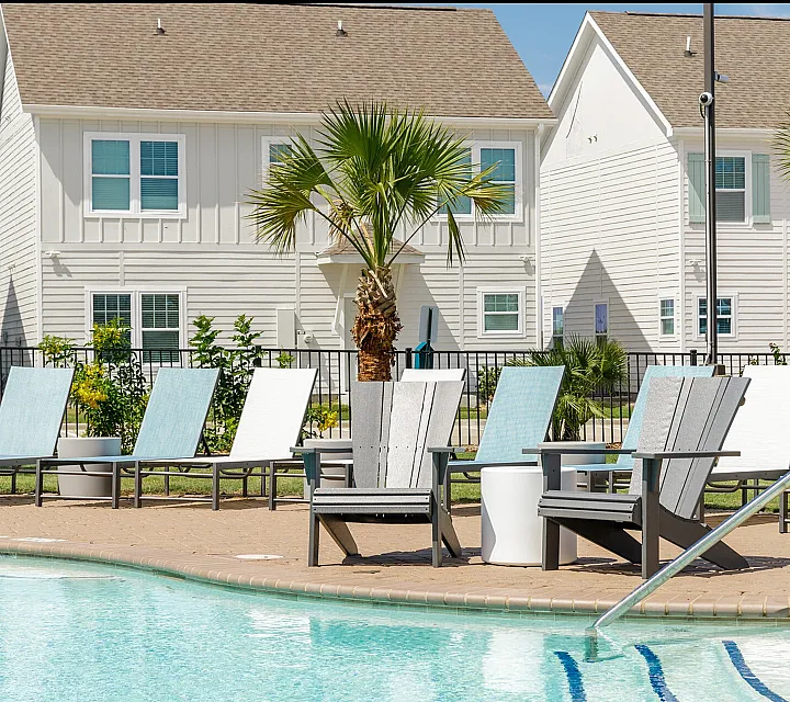 Inviting outdoor pool area with comfortable lounge chairs, palm trees, and charming white townhouses in the background.