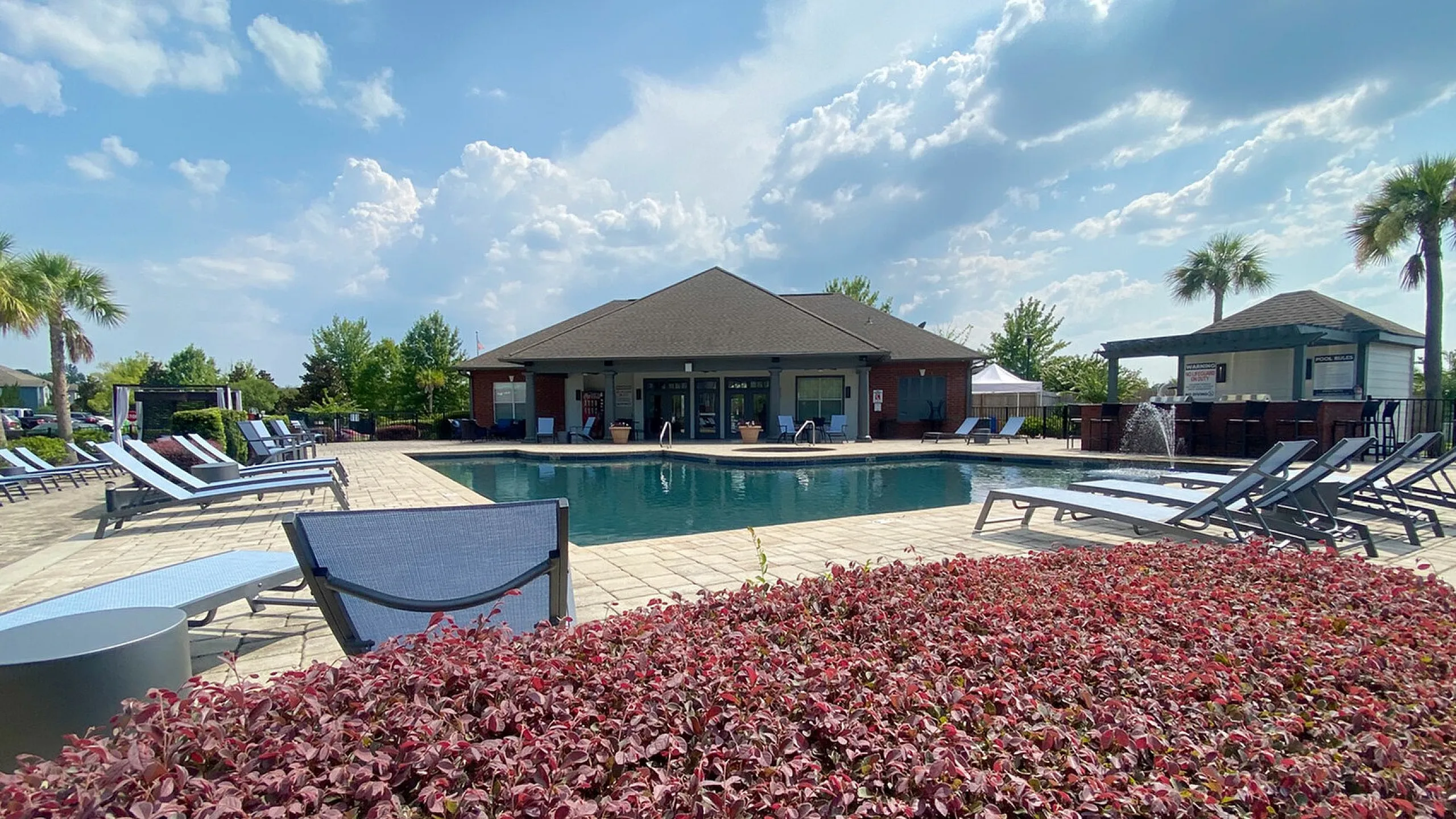 Luxurious poolside view featuring a sparkling swimming pool, stylish lounge chairs, and lush landscaping under a bright blue sky.