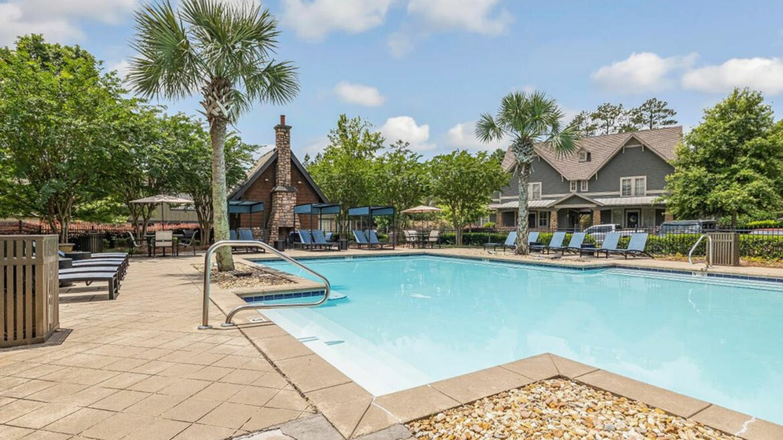 Inviting outdoor pool area with sun loungers, surrounded by lush greenery and charming architecture, perfect for relaxation.